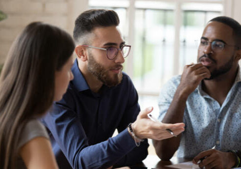 In board room gathered multi racial business people focus on serious middle eastern ethnicity team leader talking about strategy, corporate goals, share ideas, solve problems together at group meeting